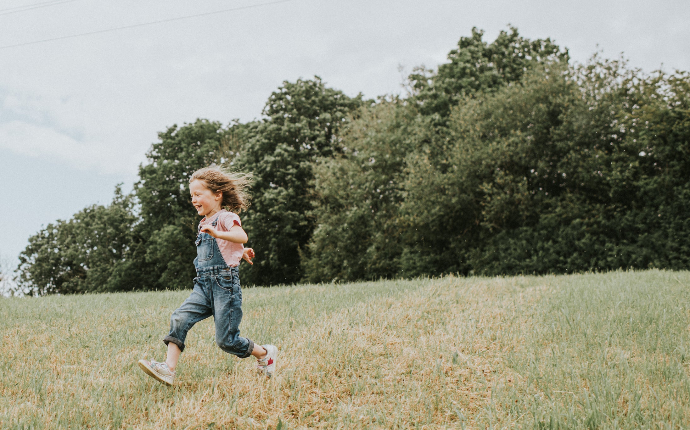 Cute little girl runs as fast as her little legs can take her across a large grassy area. She laughs as she does so. Space for copy.