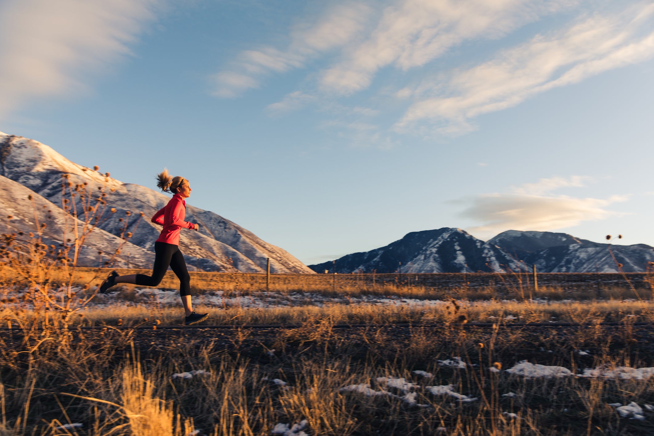 A female runner runs along a suburban footpath at sunset. Snow is still on the ground, but the partially cloudy skies and warmer temperature is great running weather. She is training for the upcoming races of the new year and to accomplish her new years resolutions.Photograph taken in Utah, USA.