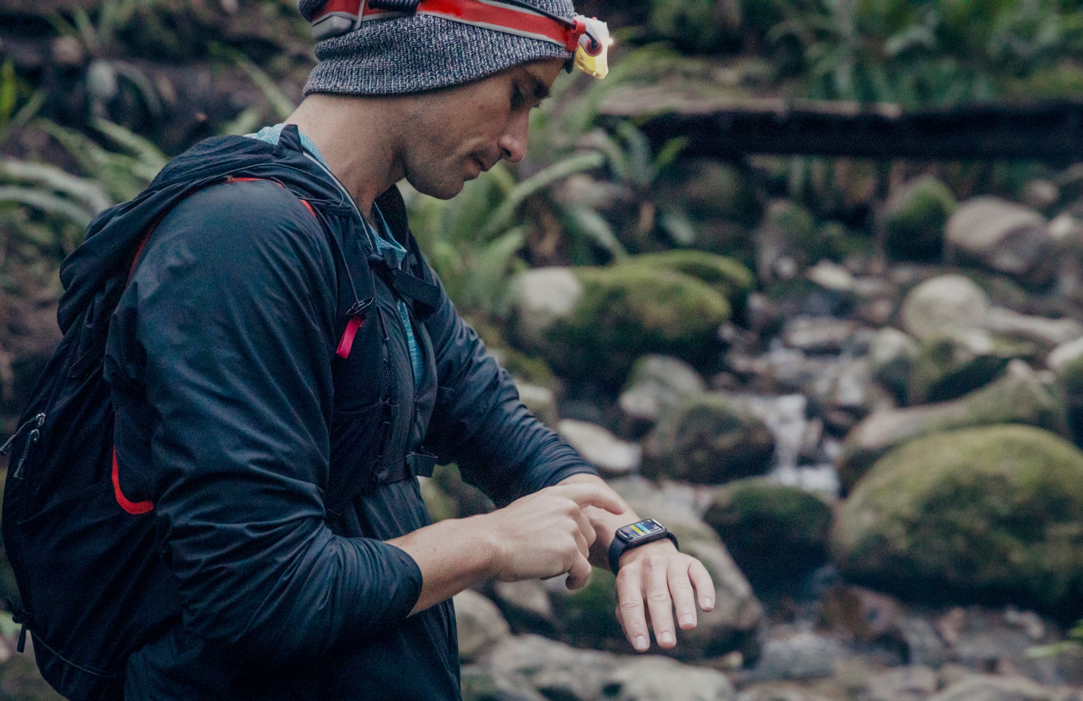 A male runner stops during a forest run to monitor vital health information on his smart watch