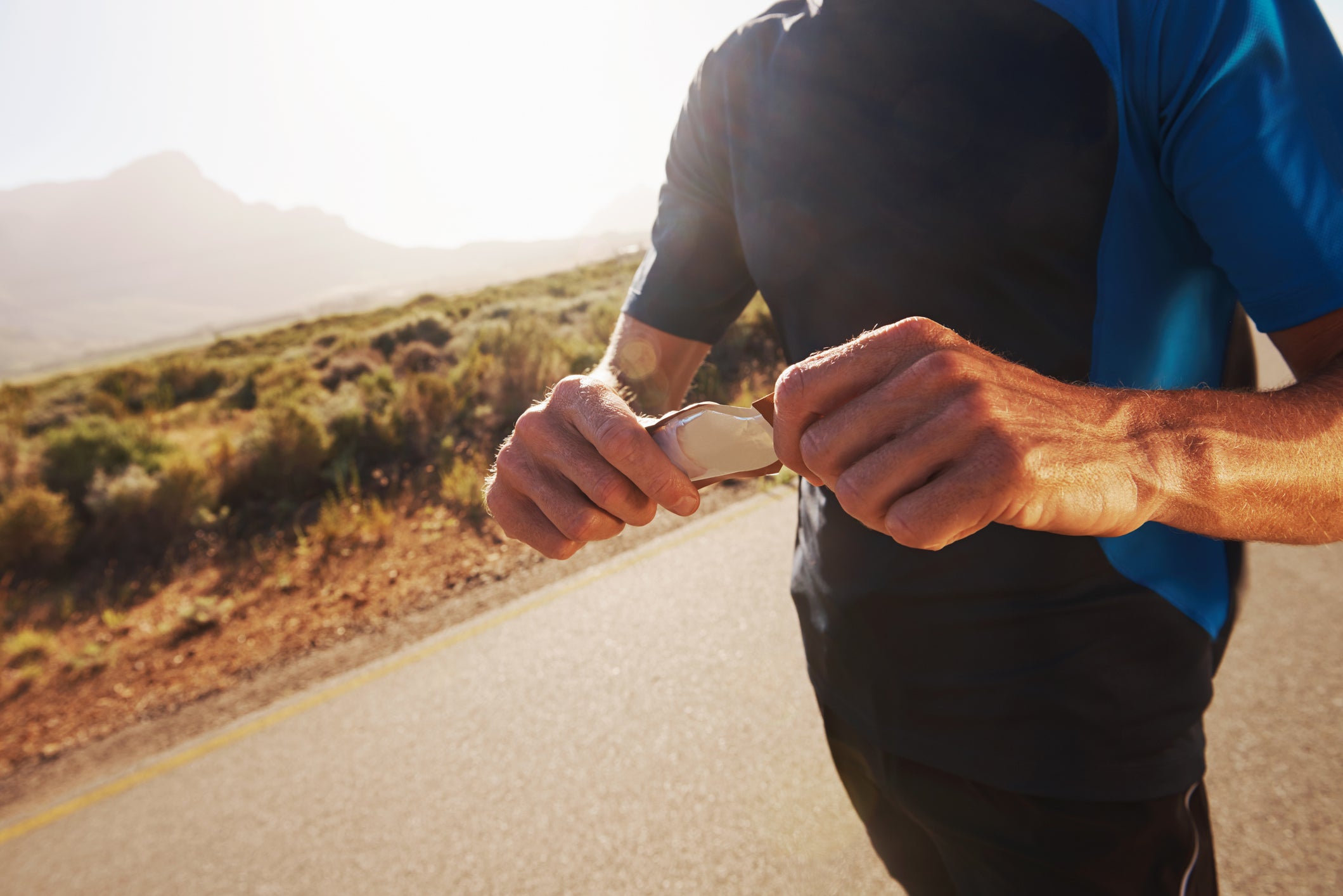 Cropped closeup shot of a male runner unwrapping an energy gel while out on a run in the country