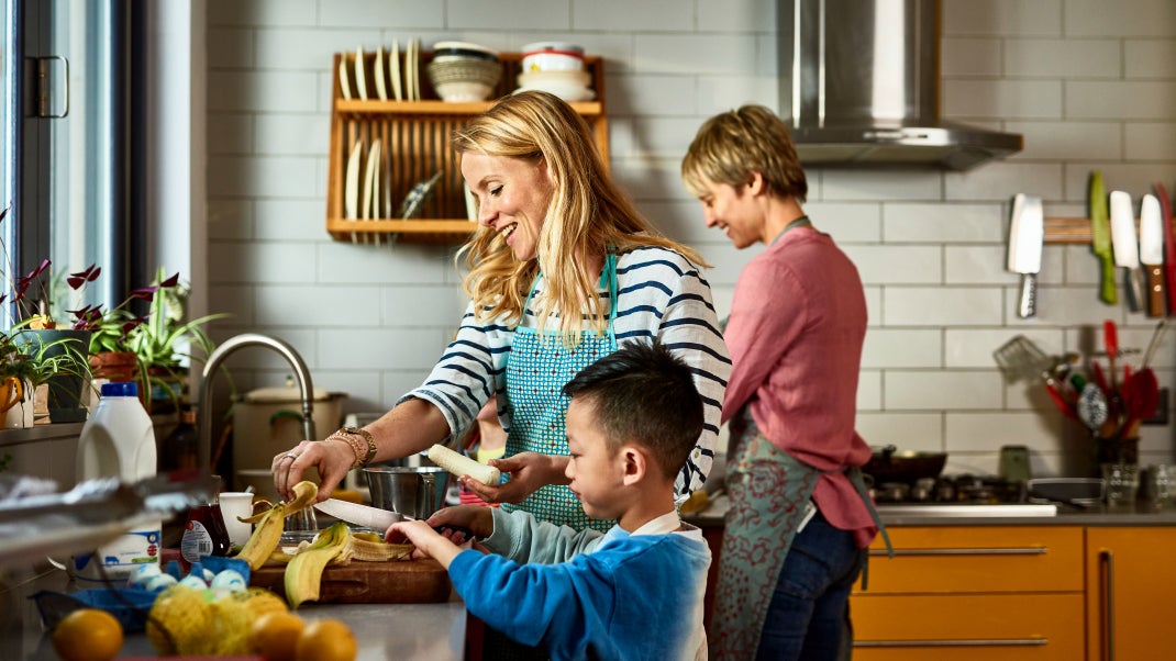 Cheerful lesbian couple preparing food with adopted son in kitchen, learning, sharing, encouragement