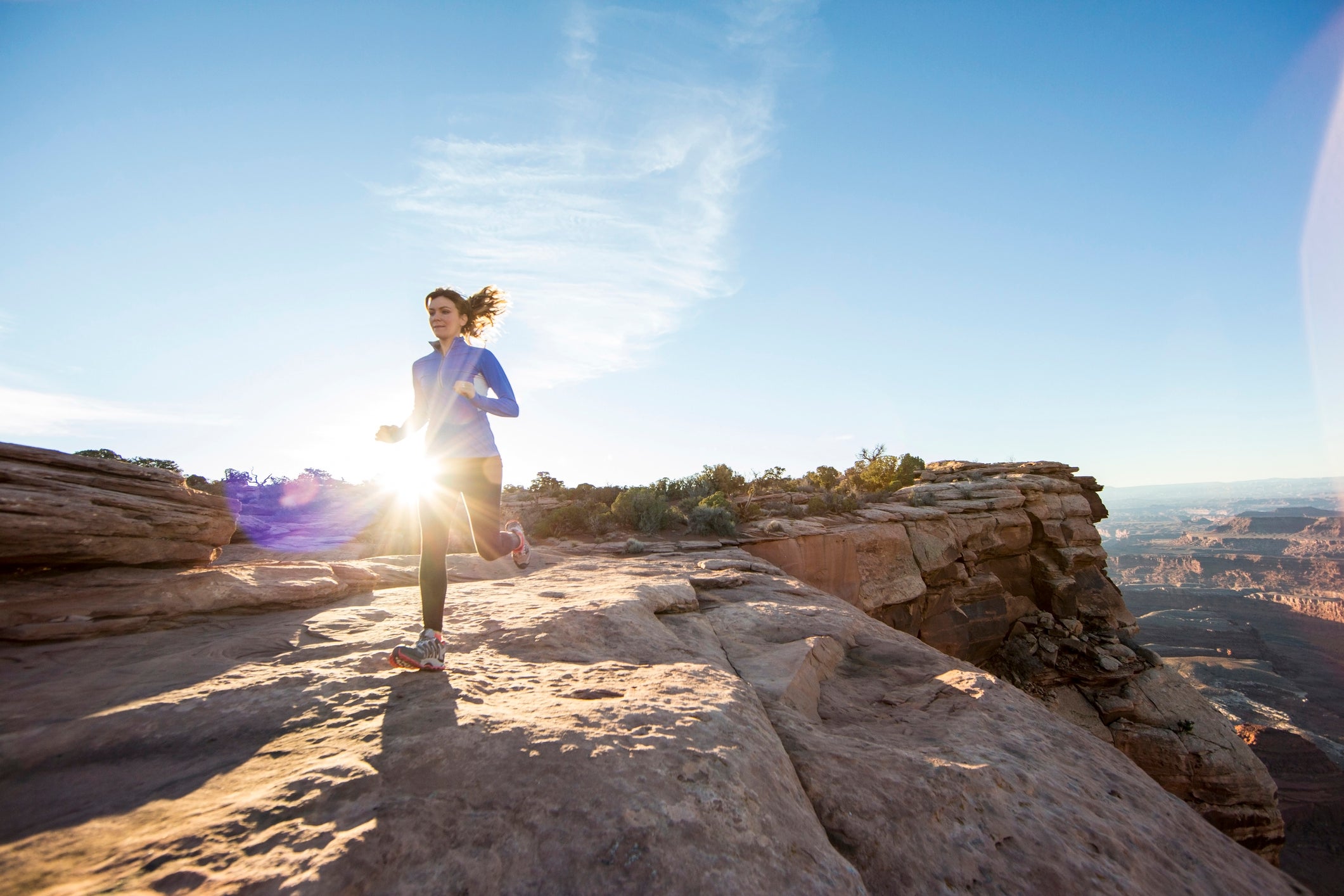A young woman trail running on top of a cliff at sunrise.