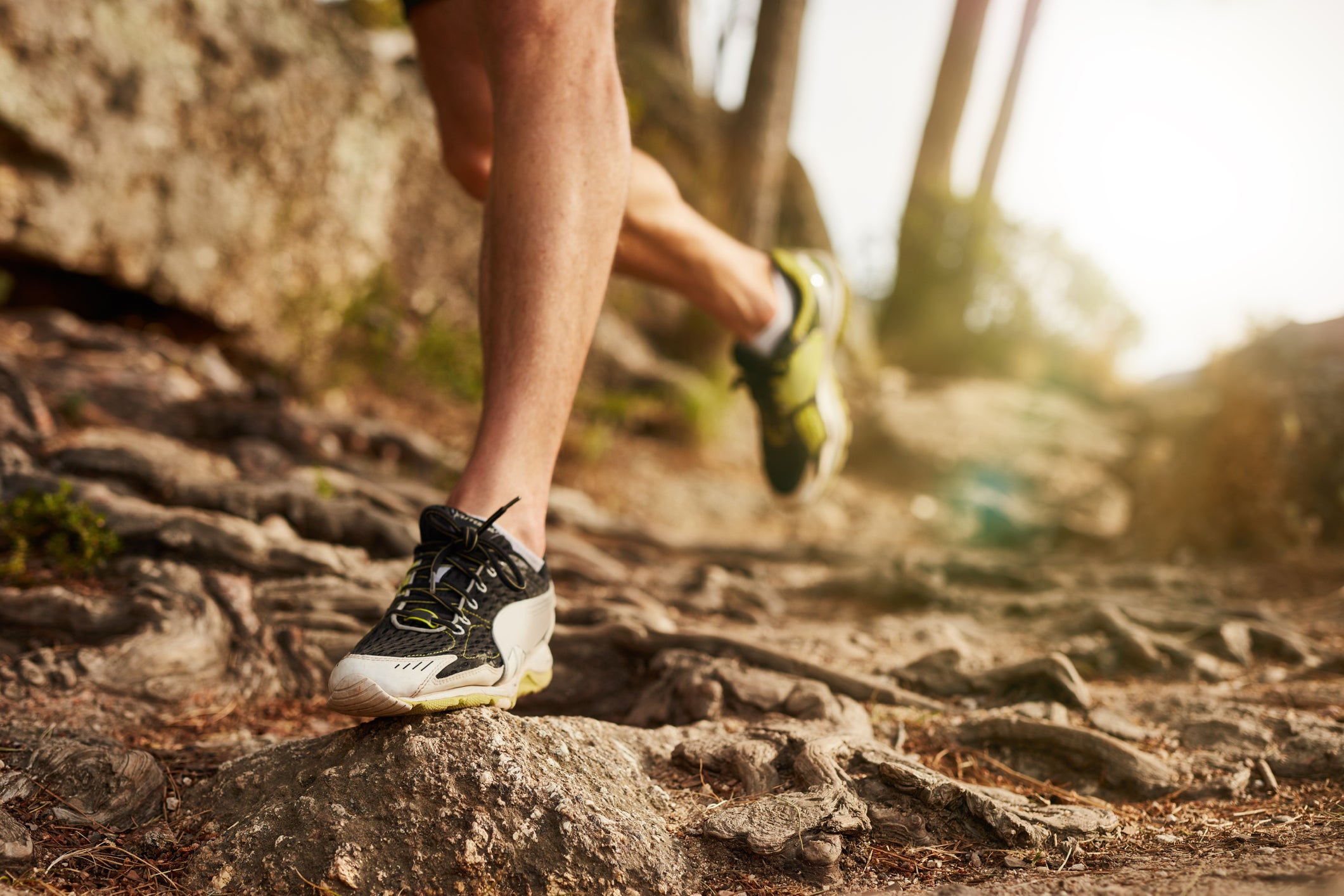 Close-up of trail running shoe on challenging rocky terrain. Male runner's legs working out on extreme terrain outdoors.