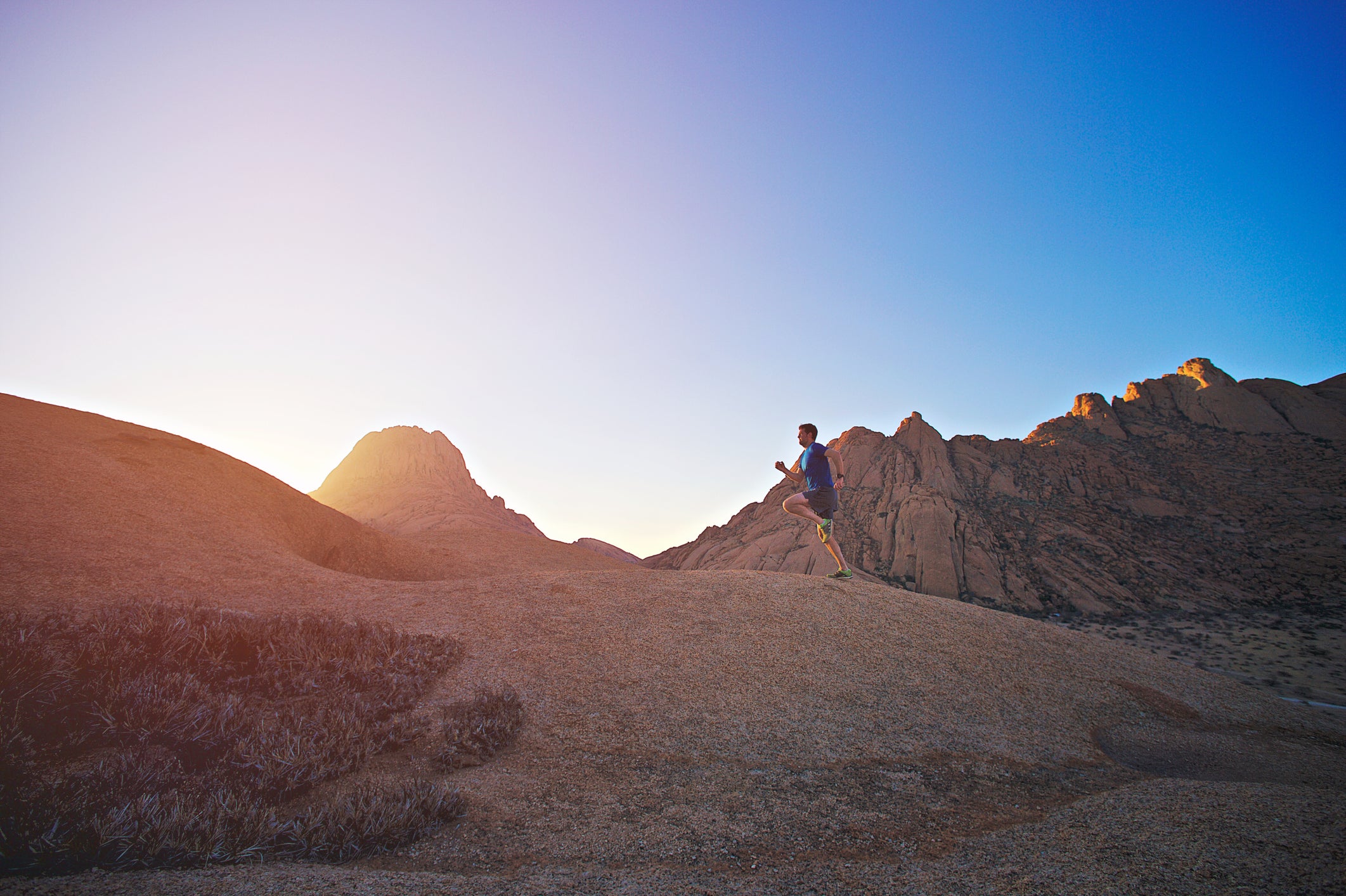 A side view of a Male trail runner running on a rock at sunset Namibian Desert Spitzkoppe Namibia Africa