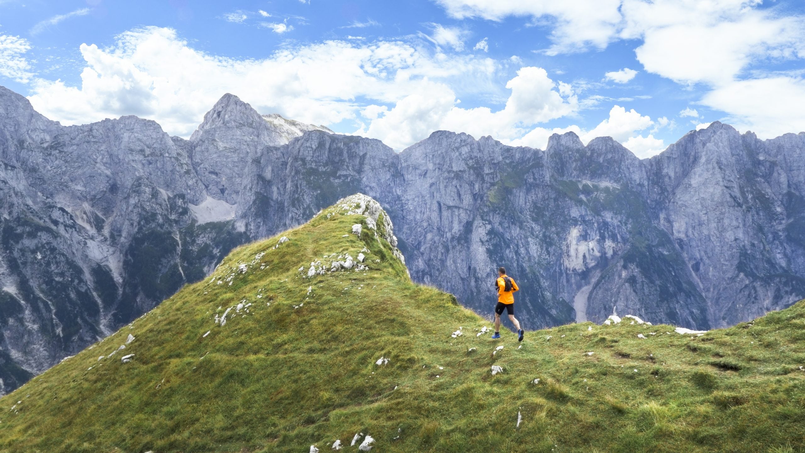 Mature man runner ascending mountain up grassy mountainside.