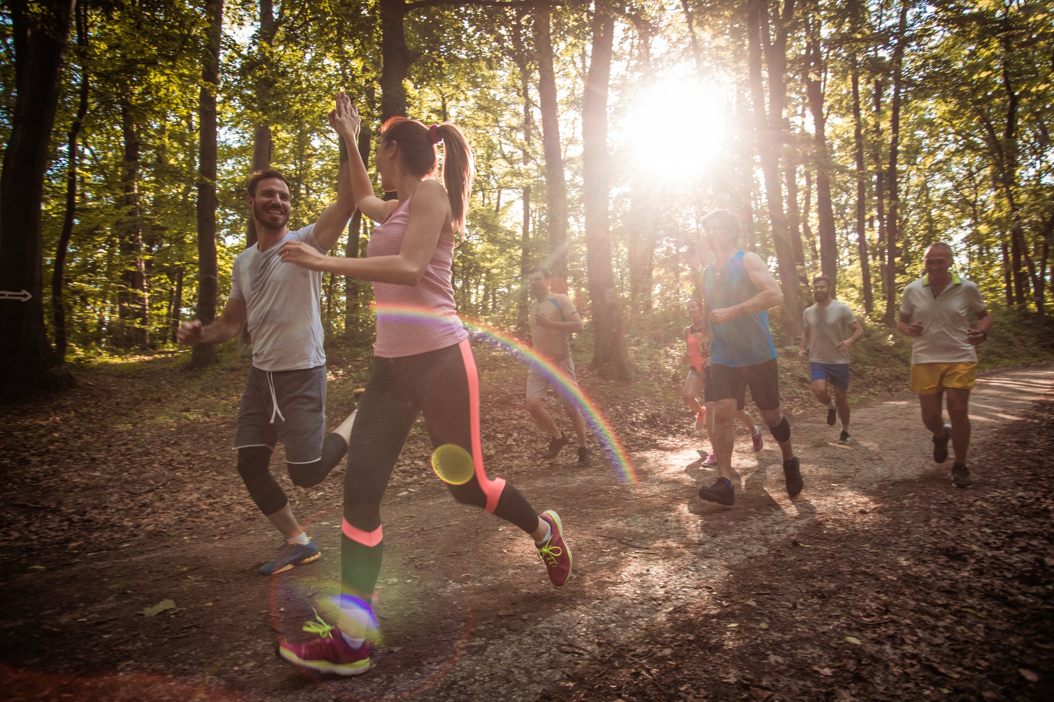 Young couple running a marathon in the forest and giving high-five to each other.