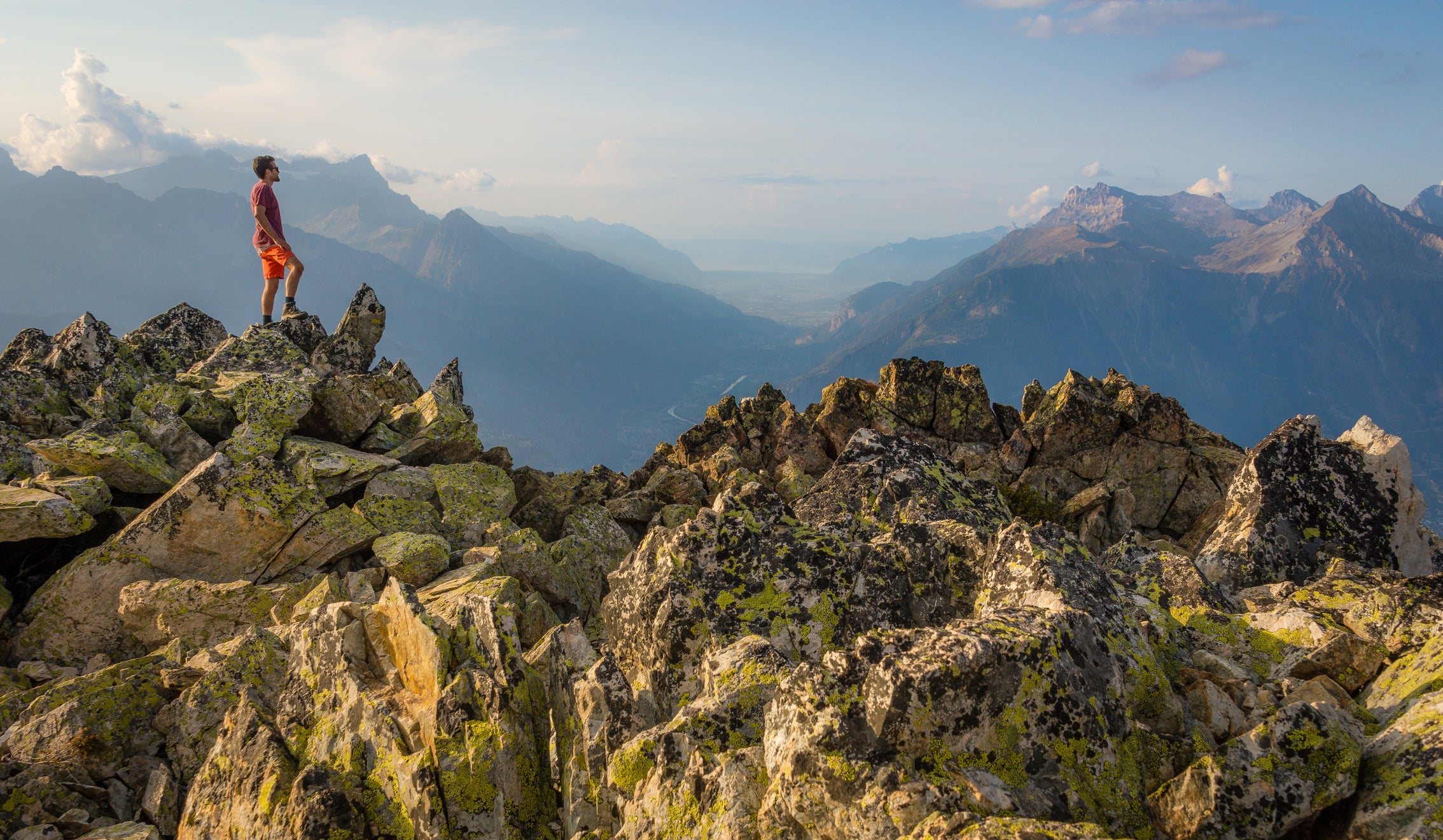 A male hiker standing on the summit of a mountain with sunset in the background.