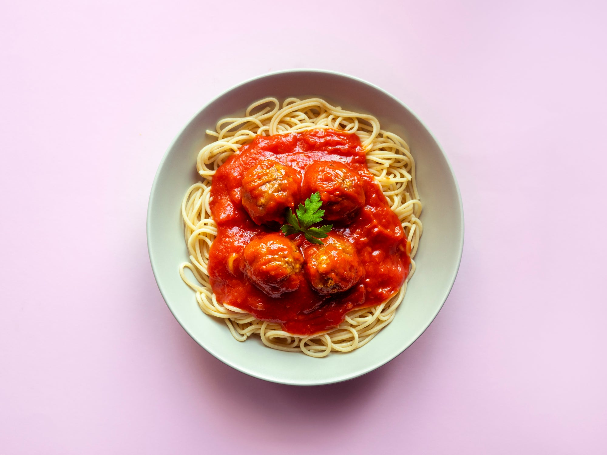 Spaghetti with meatballs and tomato sauce on pink background