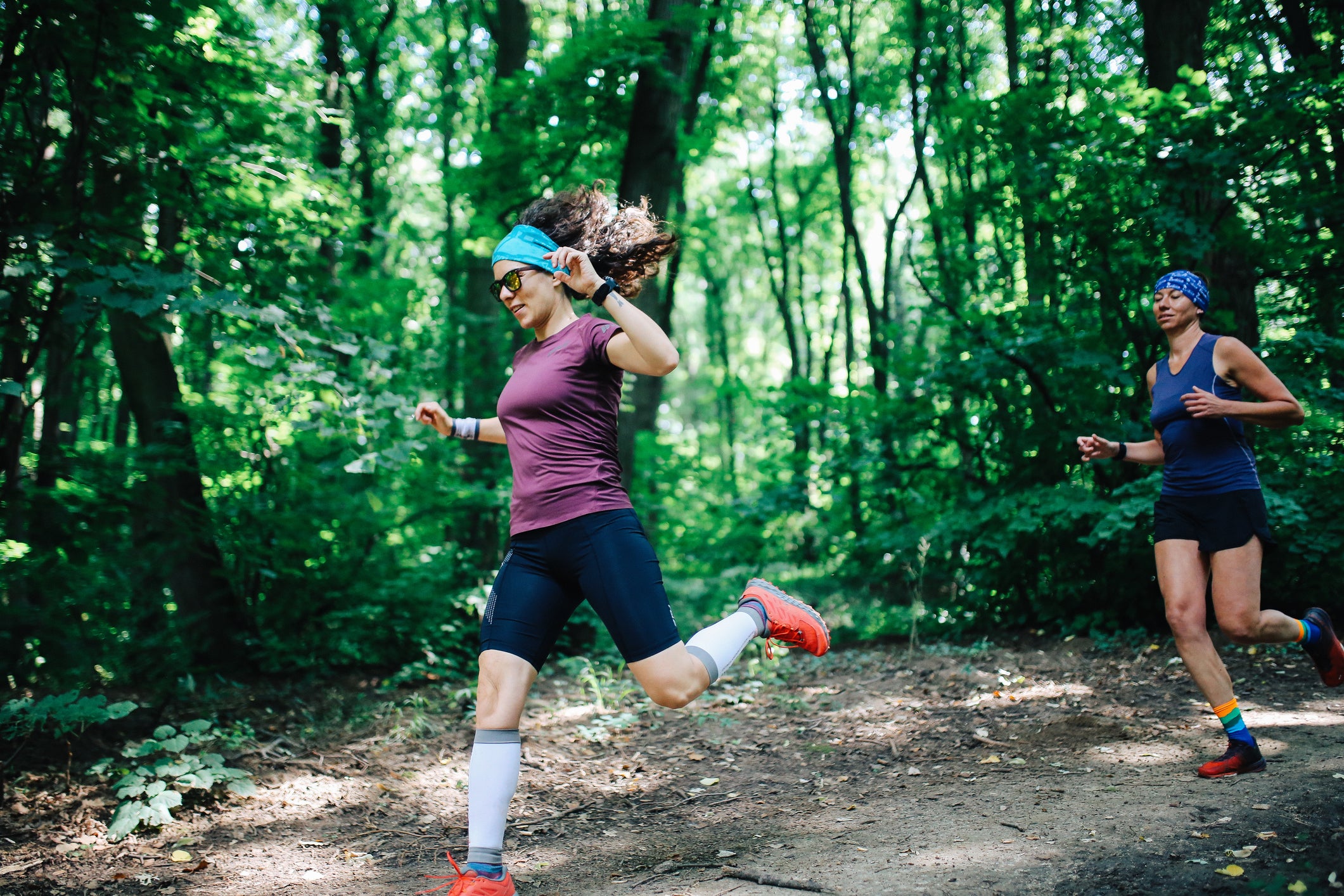 Two female athletes running in the forest.