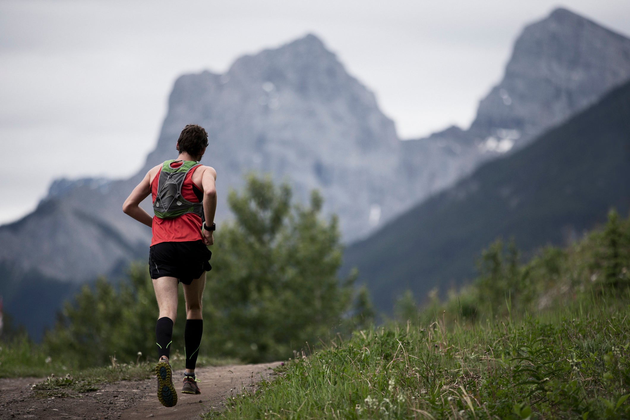 A man competes in a long distance cross country trail running race in the Rocky Mountains of Canada. He wears compression socks and a hydration back pack.