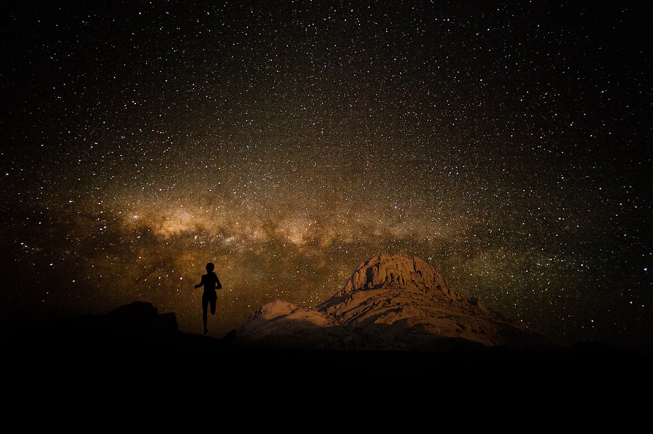 Silhouette of the back of a young female runner running away towards a spectacular star Milky Way and part of moonlit mountain Namibian Desert Spitzkoppe Namibia Africa
