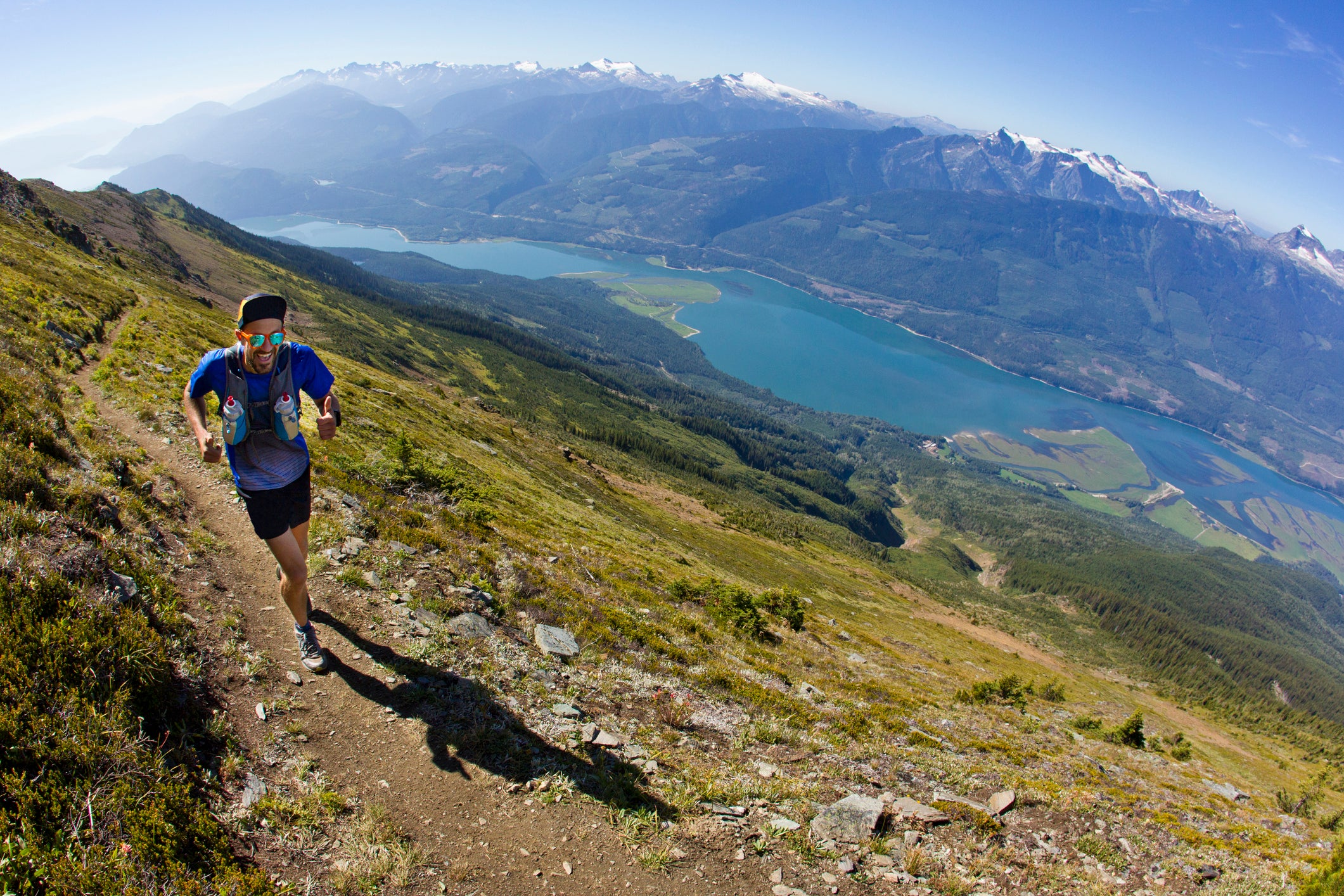 A man goes trail running near Revelstoke, British Columbia, Canada. He is wearing a running vest that carries two water bottles.
