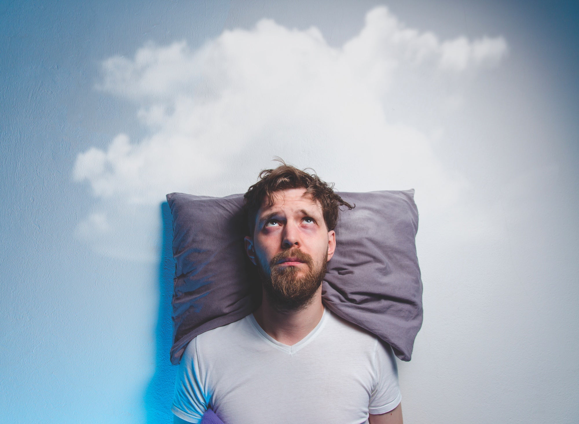 Man having problems/ insomnia, laying in bed on pillow, looking up to gray cloud over his head, copy space