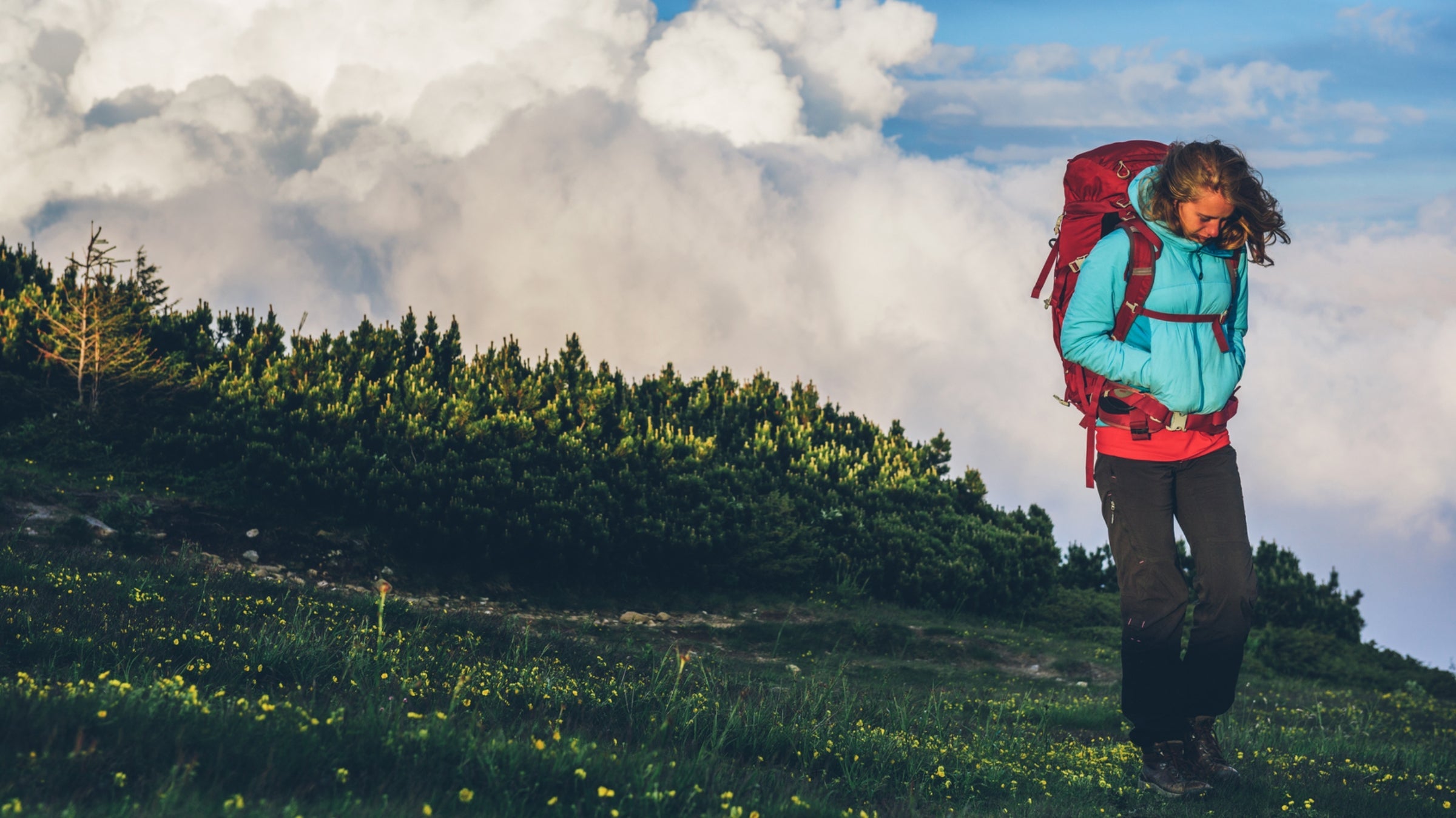 A woman cries while hiking in green tundra terrain.