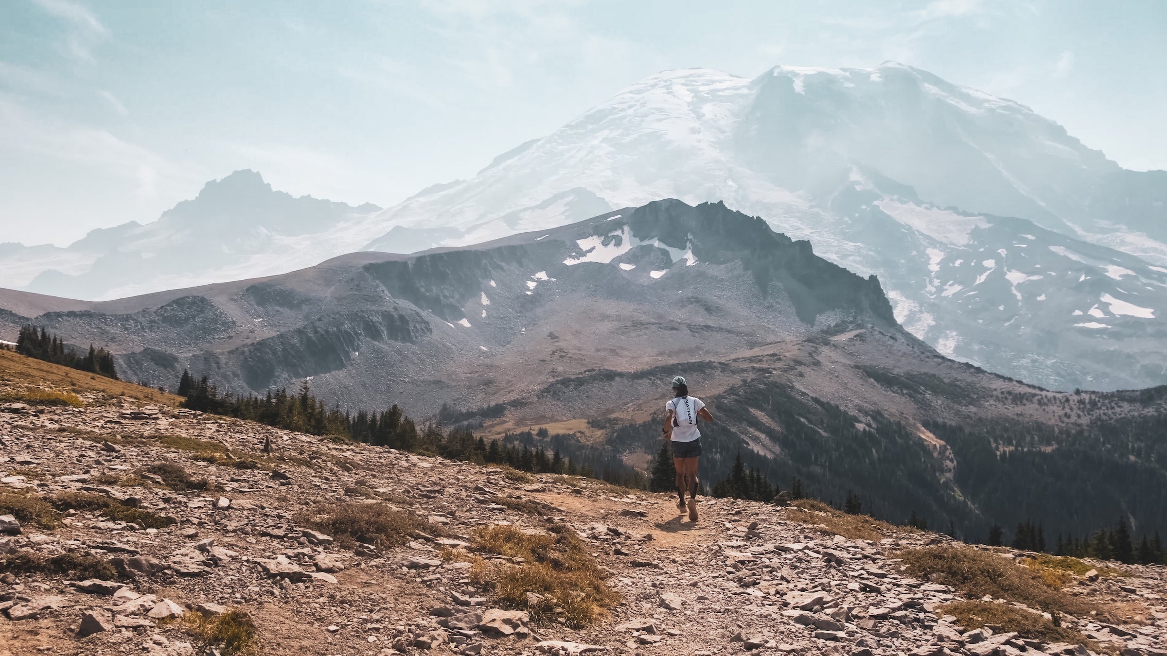 A runner moves along a trail toward a large mountain in the background