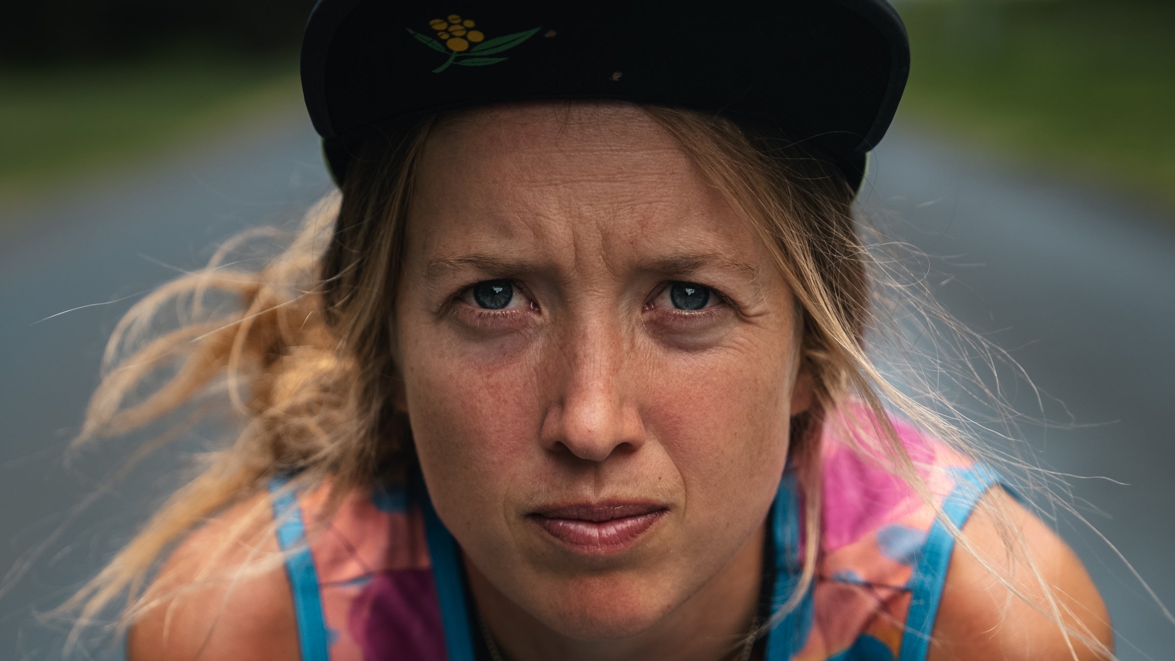 a female runner with a hat on wears pink singlet and looks into the camera