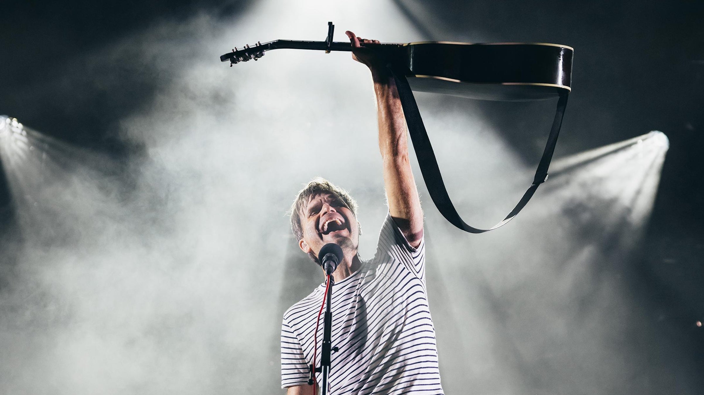 A musician holds up his guitar on stage to a smoke filled background