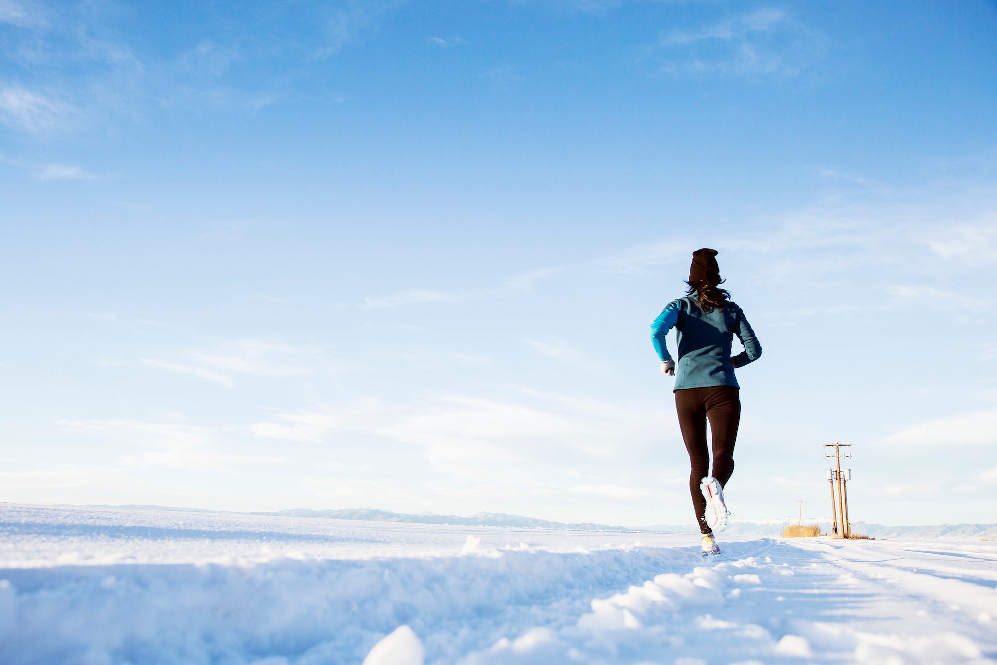 a woman is running on the snow in Colorado, wearing blue and a black pack.