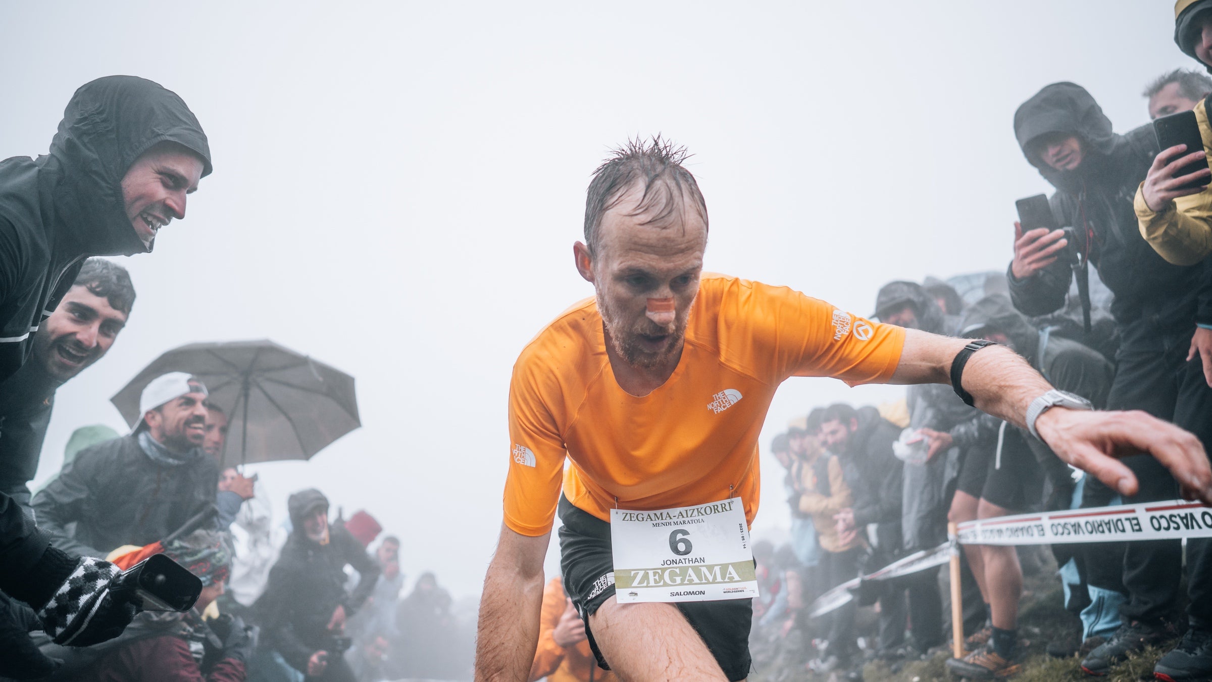 A man in orange hikes up a steep wet section of trail