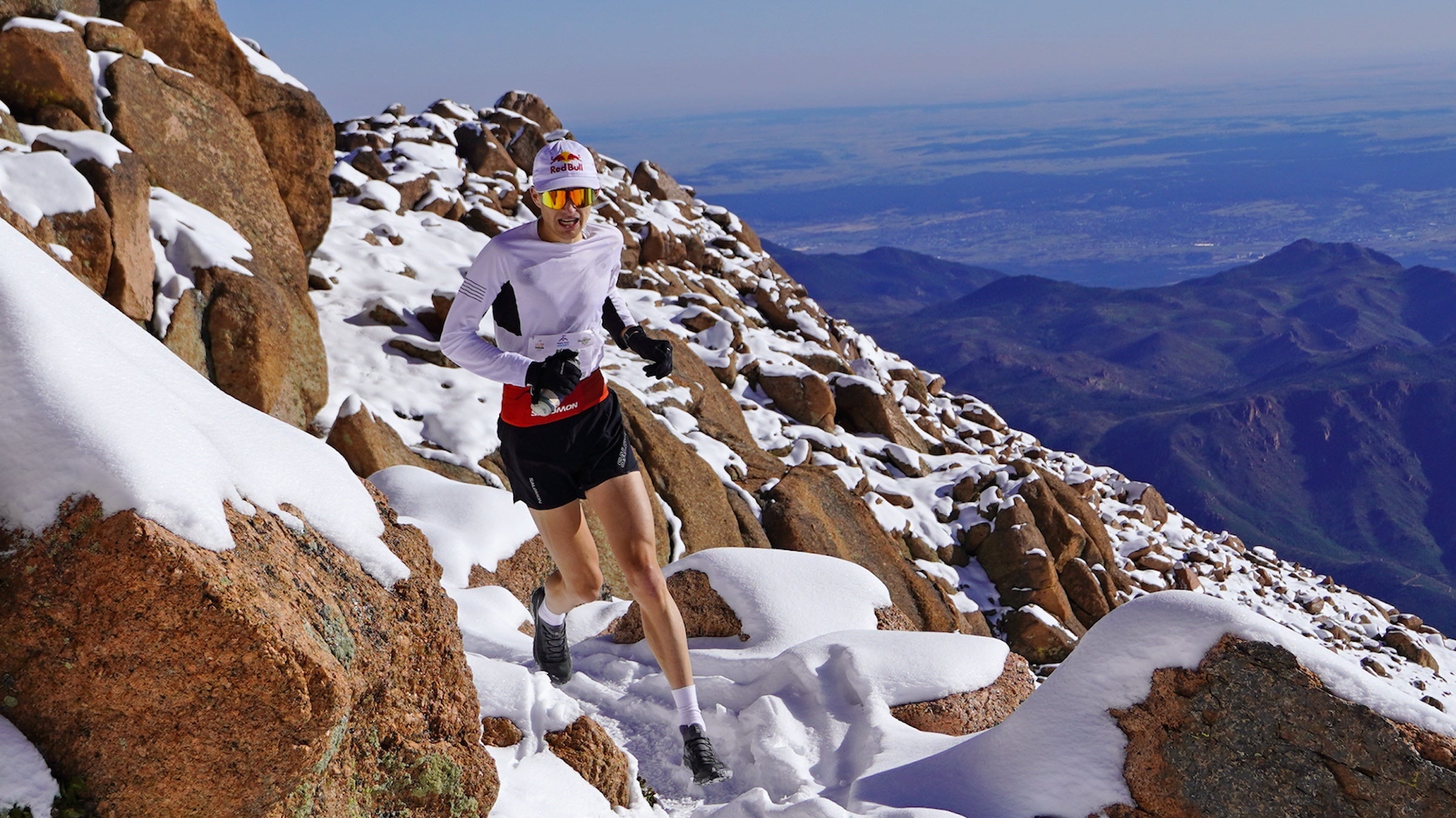 A man in white runs up a trail in the snow