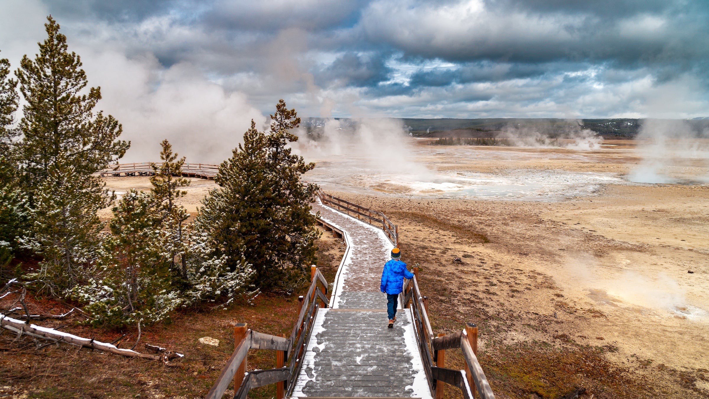 a boy walking down the stairs on a boardwalk over geothermal springs